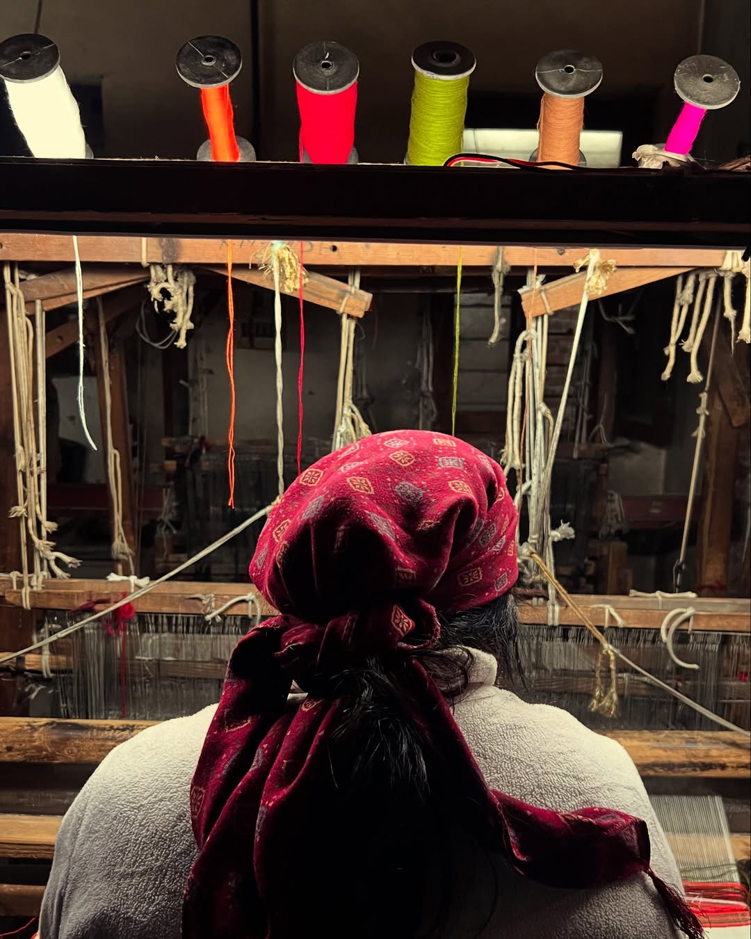 A craftswoman weaving beneath bright spools of yarn